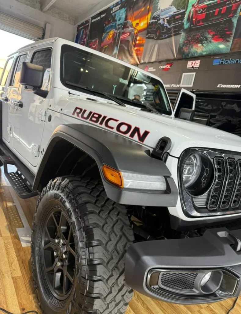 White Jeep Wrangler Rubicon with dark carbon window tint inside an automotive shop