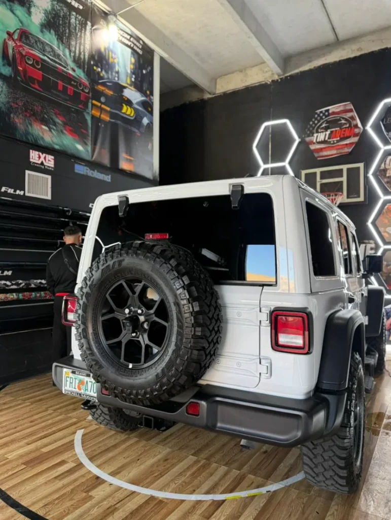 Rear view of a white Jeep Wrangler with dark carbon window tint inside an automotive tint shop